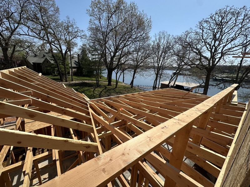 New home roof rafters framed against a clear sky with a view out to the lake